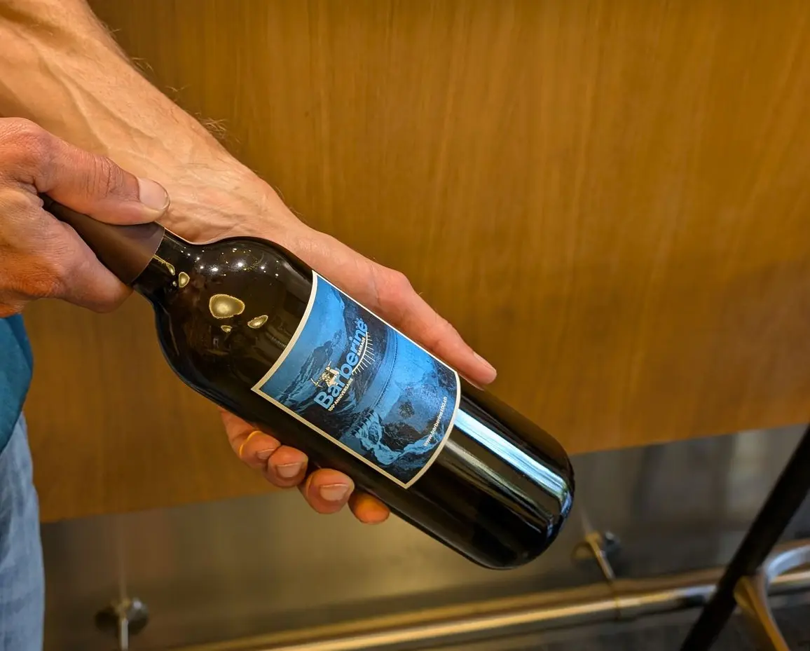 Mains tenant une bouteille de vin du Domaine Gérald Besse habillée d'une étiquette personnalisée sur mesure pour entreprise.