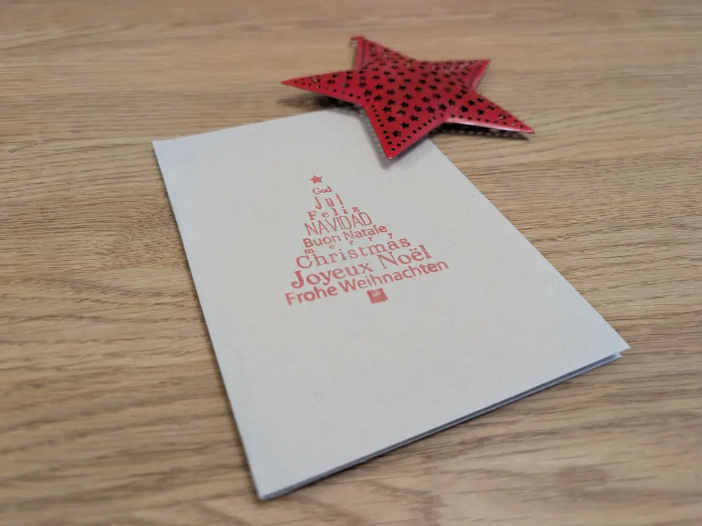Carte de vœux pliée avec motif de sapin de Noël posée à côté d'une étoile décorative rouge pour accompagnement des coffrets du Domaine Gérald Besse.